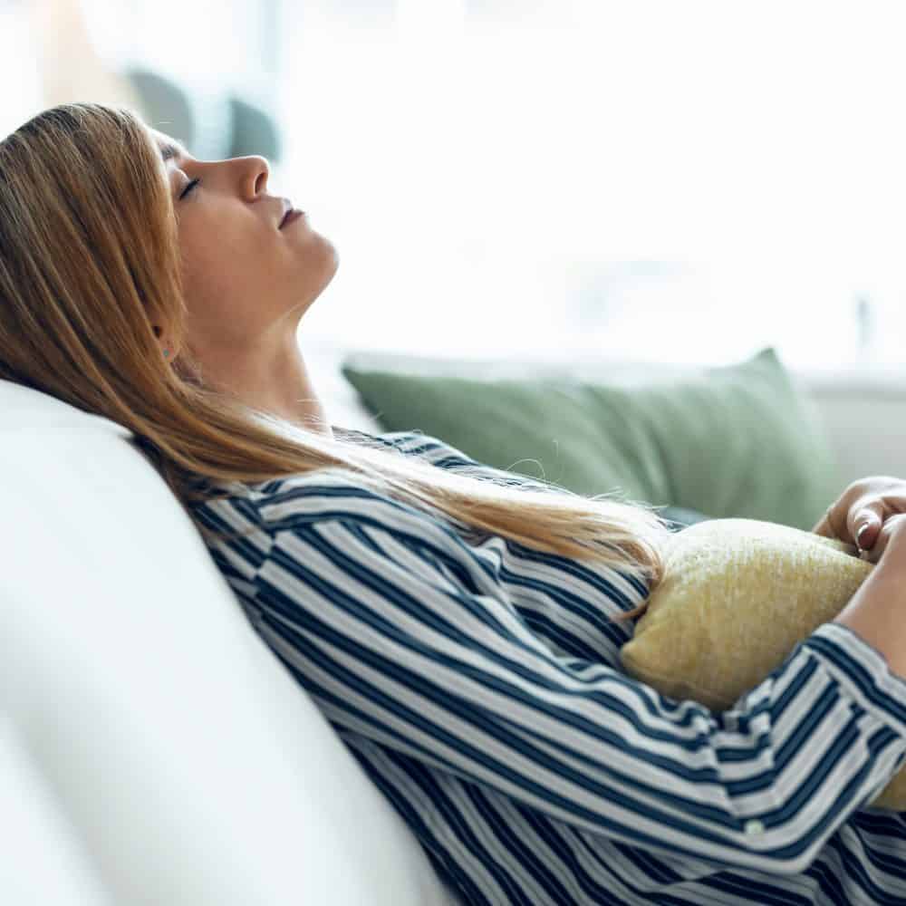 young blonde woman resting on couch with stomach problems